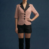 Woman wearing a pink blazer with black lapels, black shorts, and black knee-high boots on a blue background