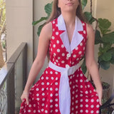 Video of a young women with long , straight light brown hair twirling in a red and white polka dot midi dress.  She is happy ands smiling.  She is on a balcony and you can see a green potted plant and part of a chair with blue cushions in the background.
